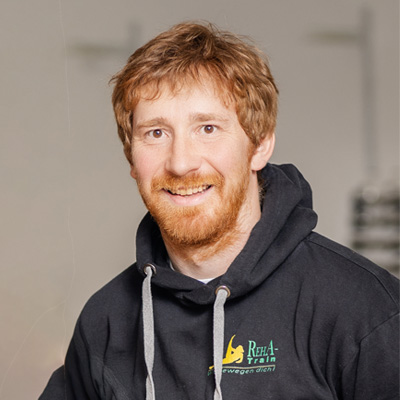 A portrait photo of Markus Kirchner with short hair and a beard. He is wearing a Reha-Train sweatshirt and smiling at the camera.