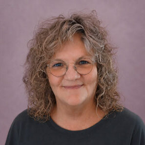 Portraitfoto von Susanne Dehring mit Brille und blondem, lockigem Haar. Sie blickt lächelnd in die Kamera.